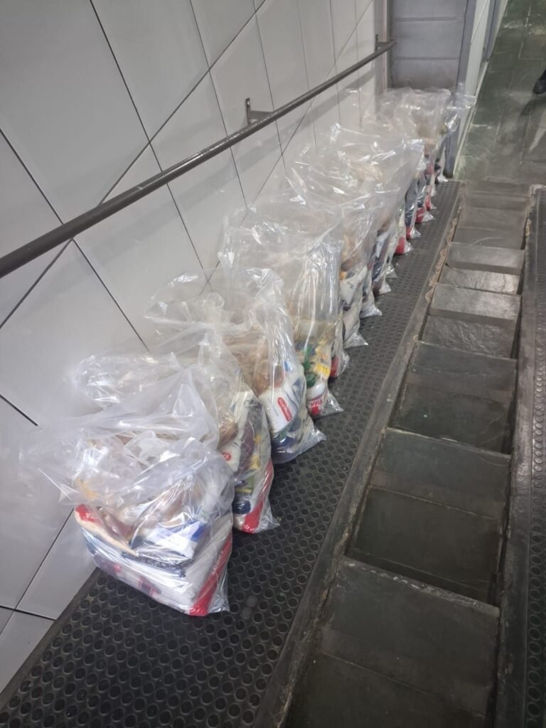 Sacolas de mantimentos já montadas e enfileiradas ao longo do corredor da casa, prontas para a entrega às famílias atendidas.